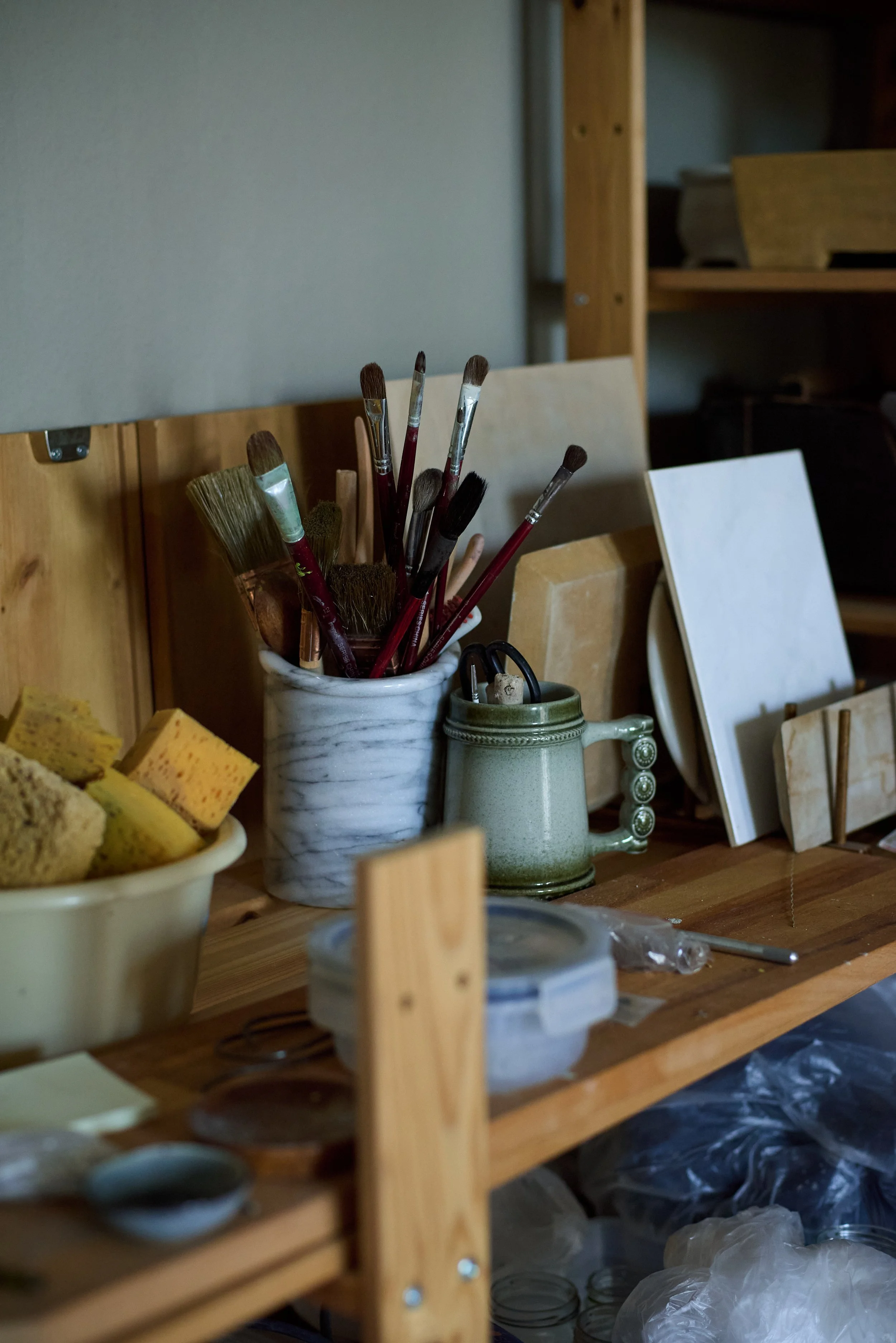 Art supplies on a wooden workspace, including paintbrushes, sponges, and canvases.