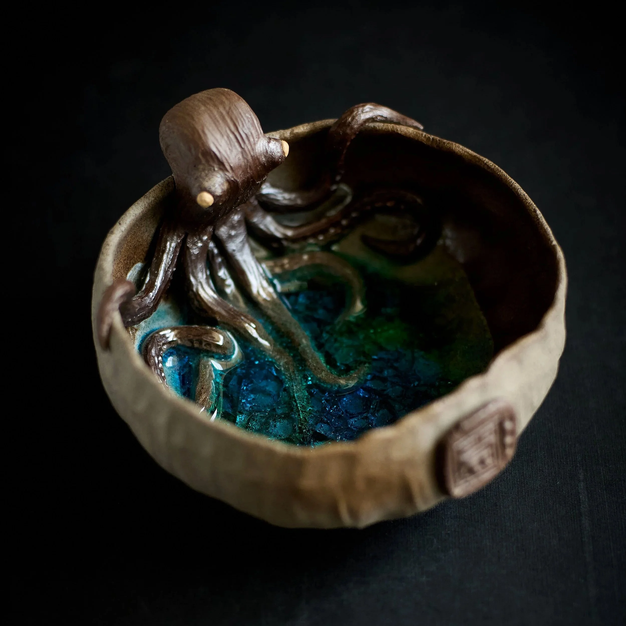 Ceramic bowl with a brown octopus decoration on the rim, filled with colorful glass pieces resembling water.