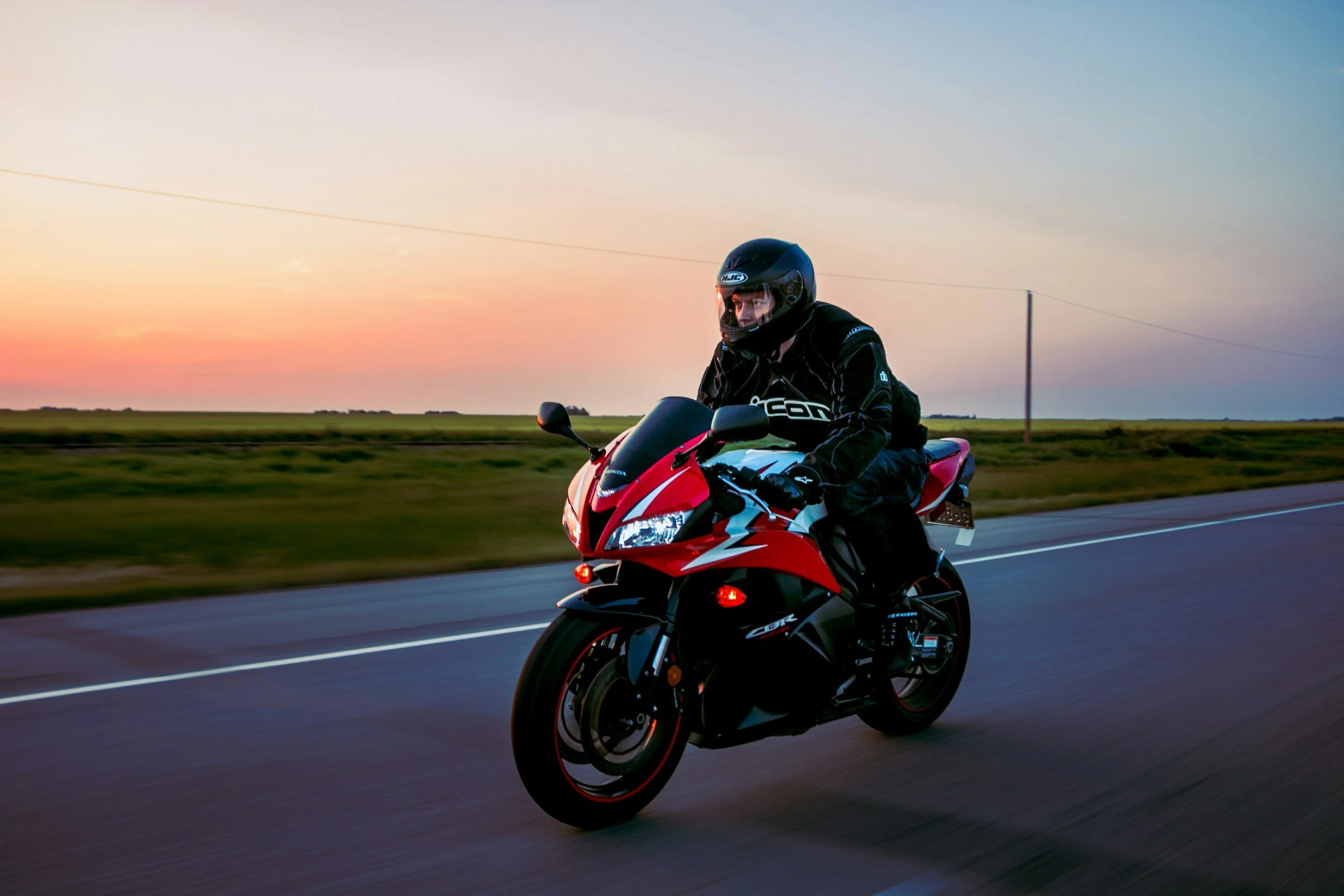 Un motard sur une moto rouge roule sur une route lors d'un coucher de soleil.