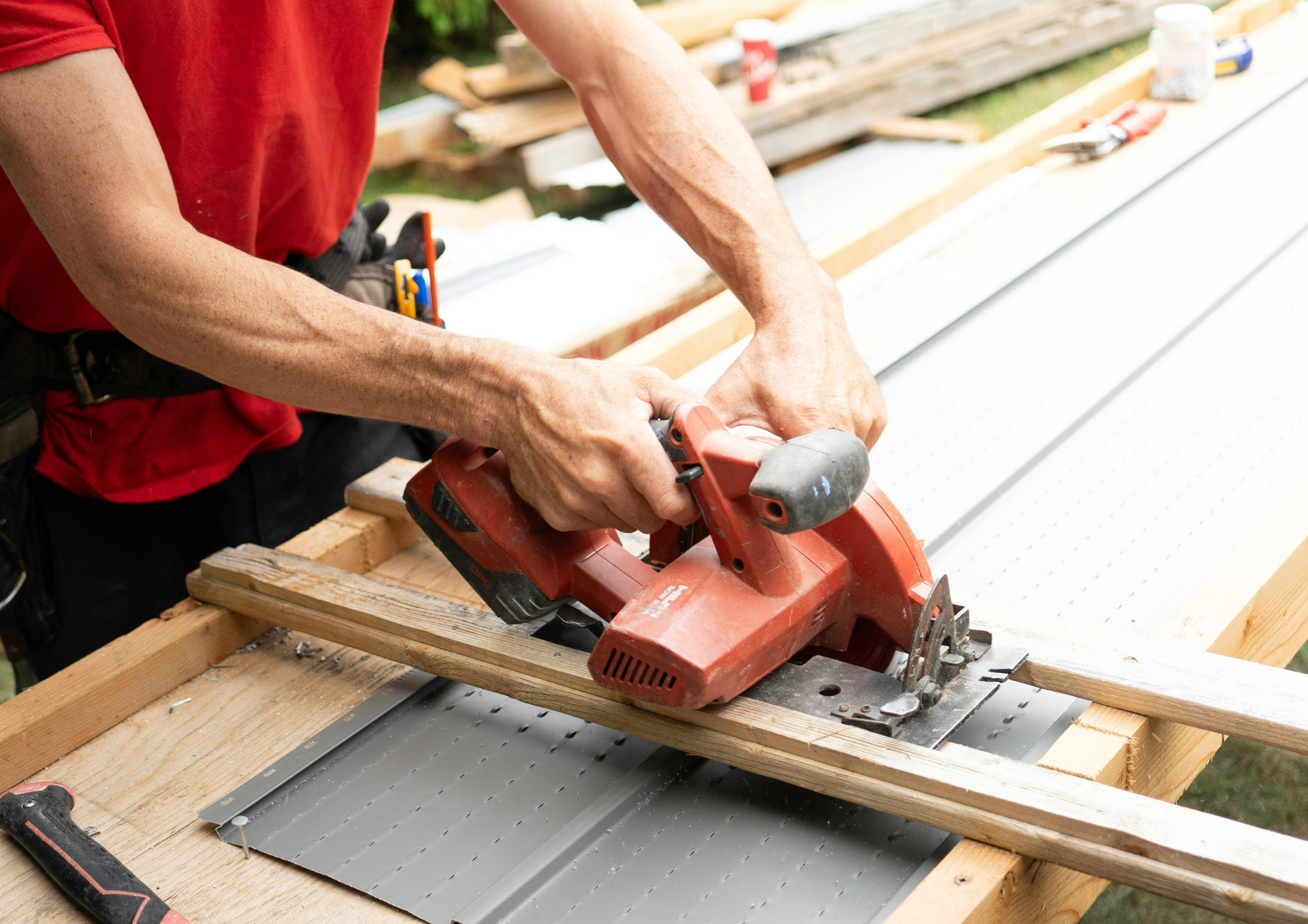Personne utilisant une scie électrique pour couper du bois sur une structure en bois, dans un environnement extérieur