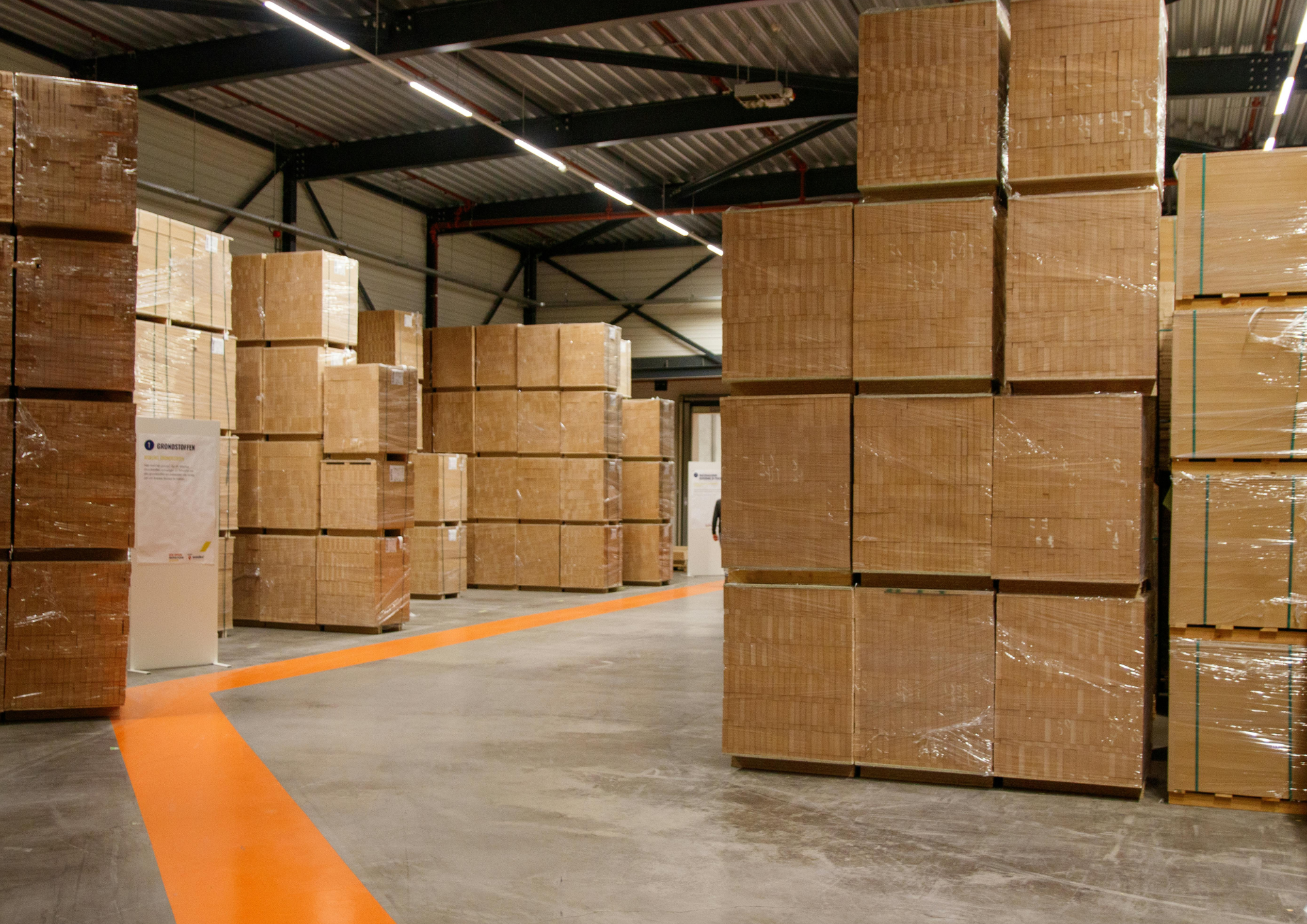 Stockage de cartons en bois dans un entrepôt, avec un sol en béton et un plafond en métal doté d'éclairage linéaire.
