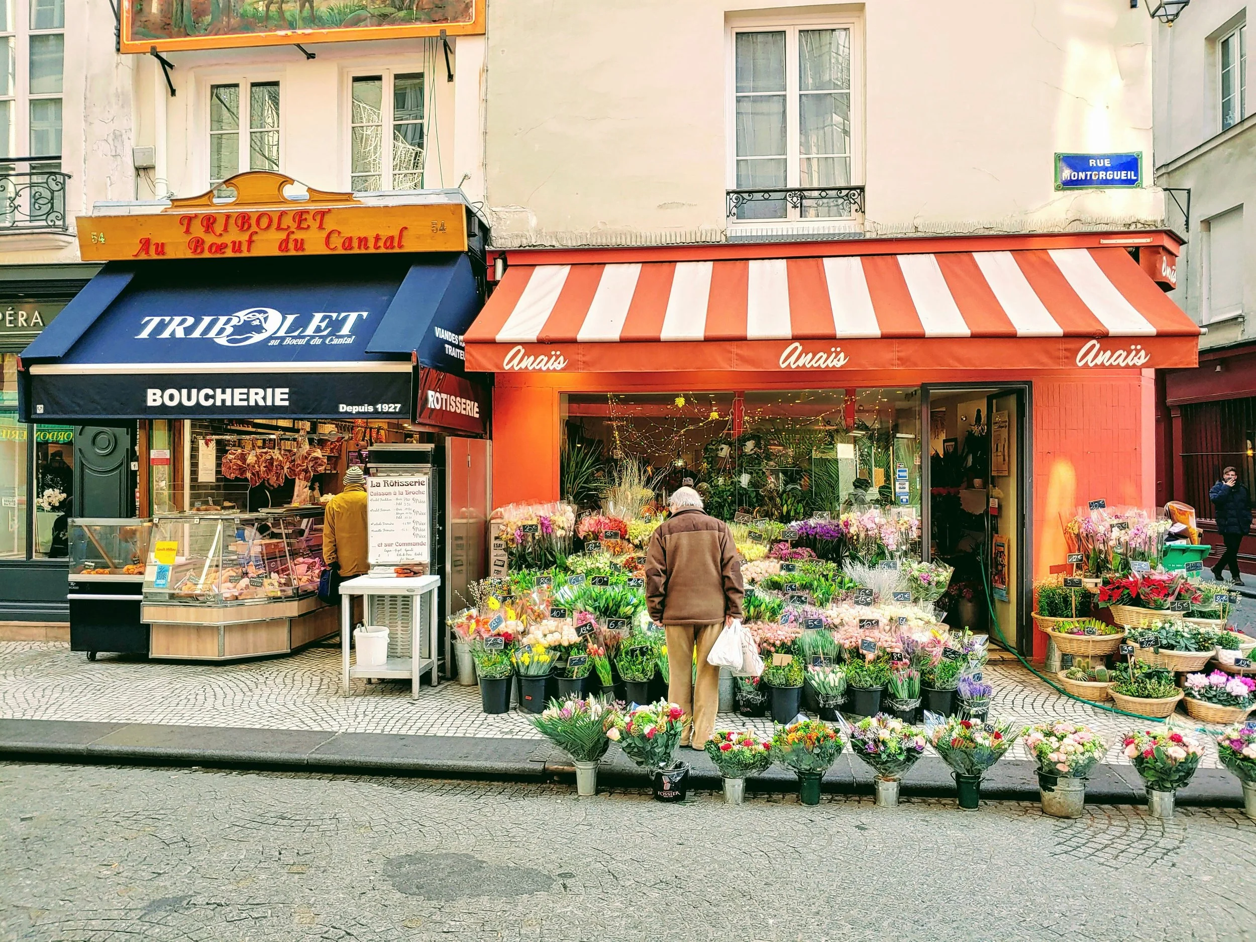 Magasin de fleurs en plein air avec des bouquets colorés devant une rue parisienne.