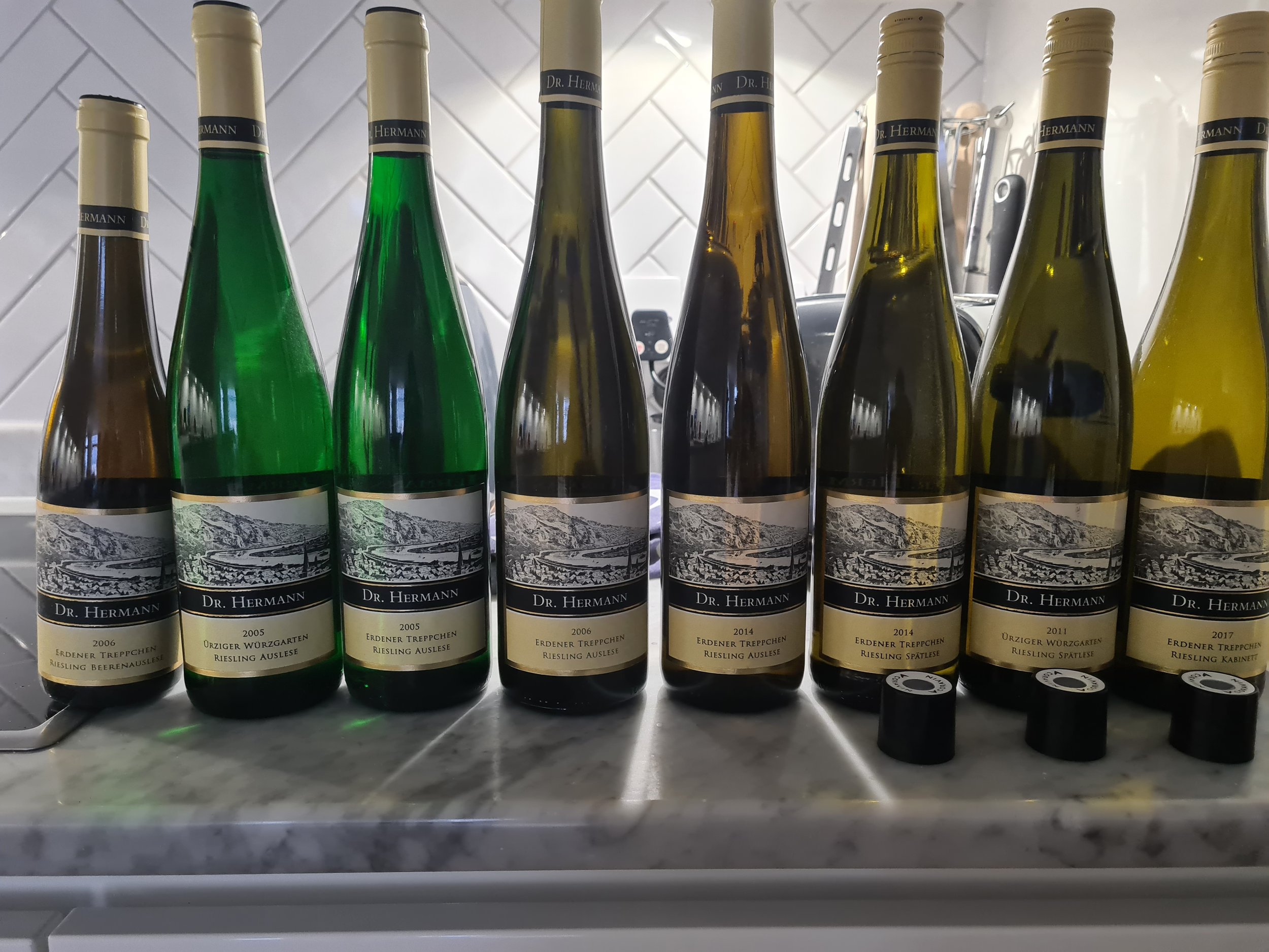 A row of ten bottles of Dr. Hermann wine on a marble surface, with labels indicating different years and types of Riesling wine, including 2006, 2005, 2014, 2017, and others.