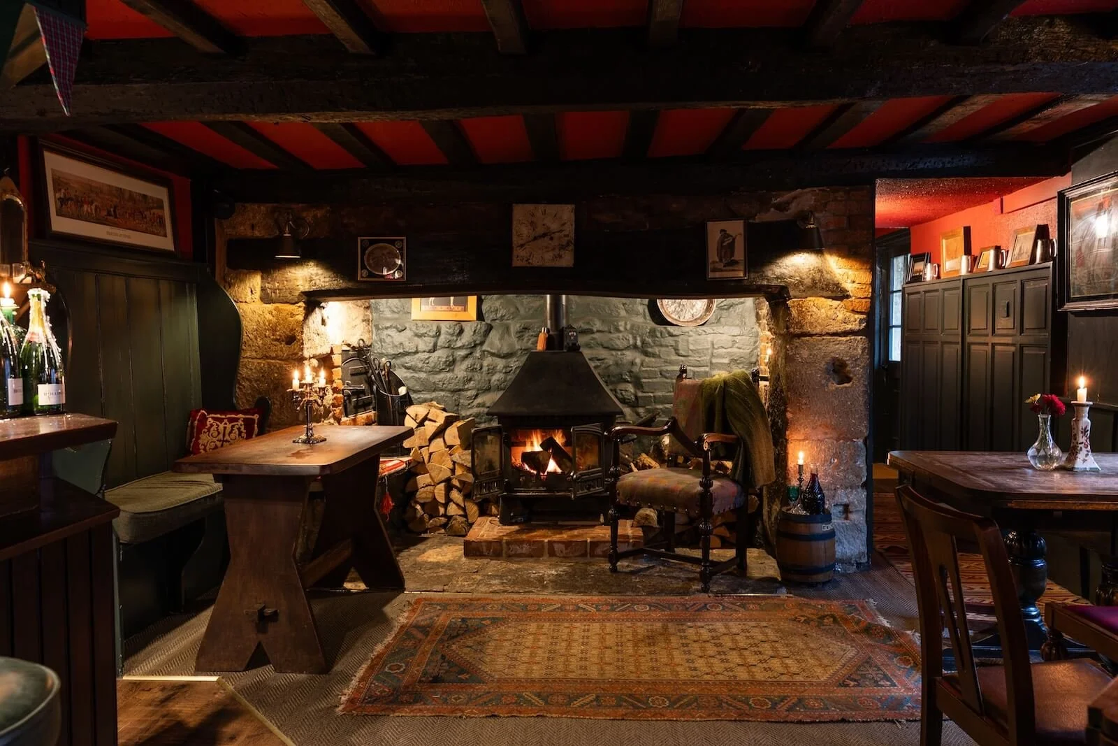 Cozy room with stone fireplace, stacked firewood, wooden furniture, candles, and rustic decor.