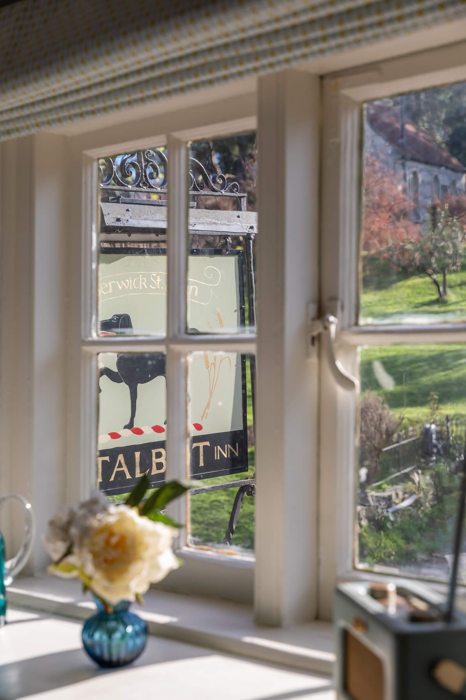View through a window showing a sign for Talbot Inn with a black duck illustration, and a scenic landscape with trees and a building outside.
