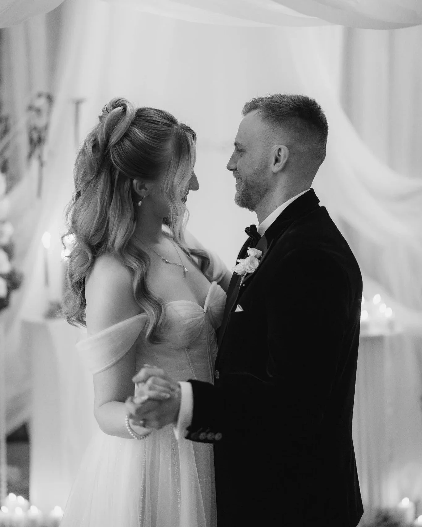 A black and white photo of a bride and groom dancing and smiling at each other during their wedding reception.