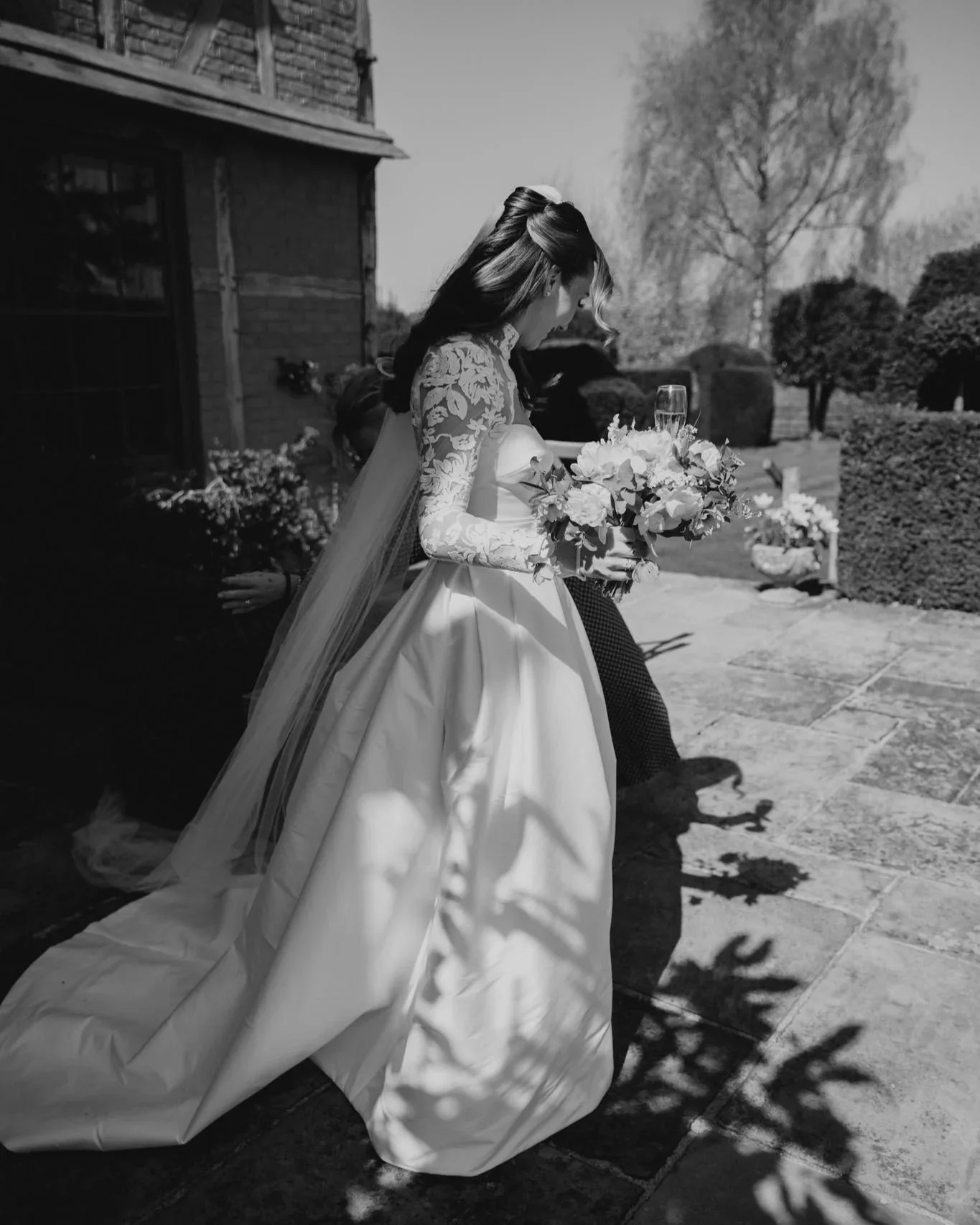 A bride in a wedding dress holding a bouquet of flowers walking outdoors on a sunny day.