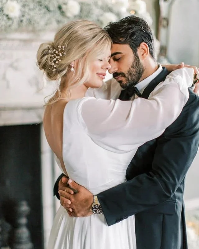 A couple dressed in wedding attire sharing a romantic embrace indoors.