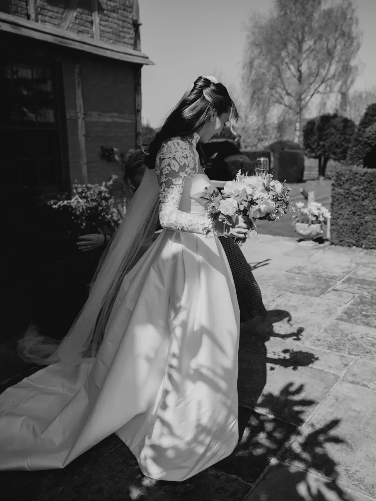 A bride in a wedding dress holding a bouquet of flowers walking outdoors on a sunny day.