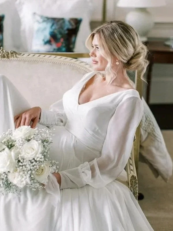 A bride in a white wedding dress sitting on a vintage sofa, holding a bouquet of white roses and baby's breath, with decorated pillows in the background.