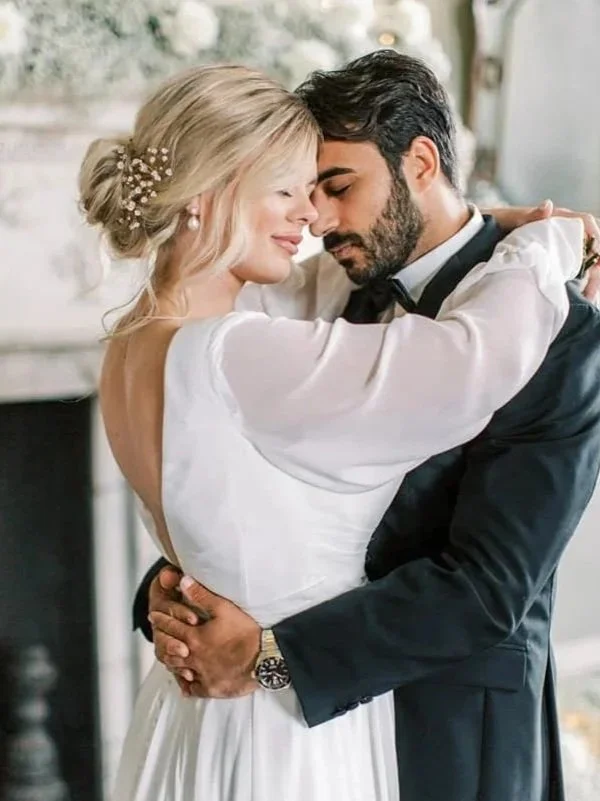 A couple dressed in wedding attire sharing a romantic embrace indoors.