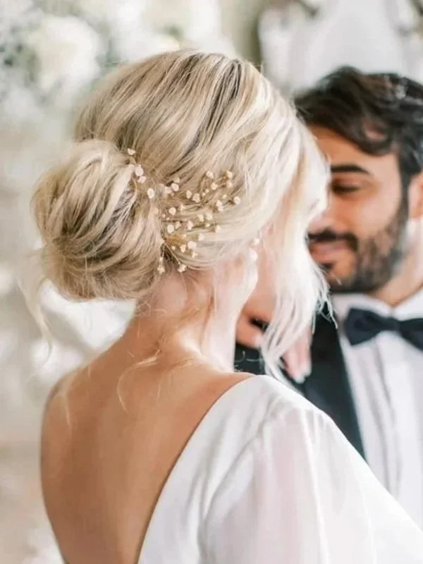 Bride and groom sharing a close, intimate moment at their wedding, with the bride's elegant updo hairstyle decorated with small white flowers and pearl accents, and the groom wearing a tuxedo with a bow tie.