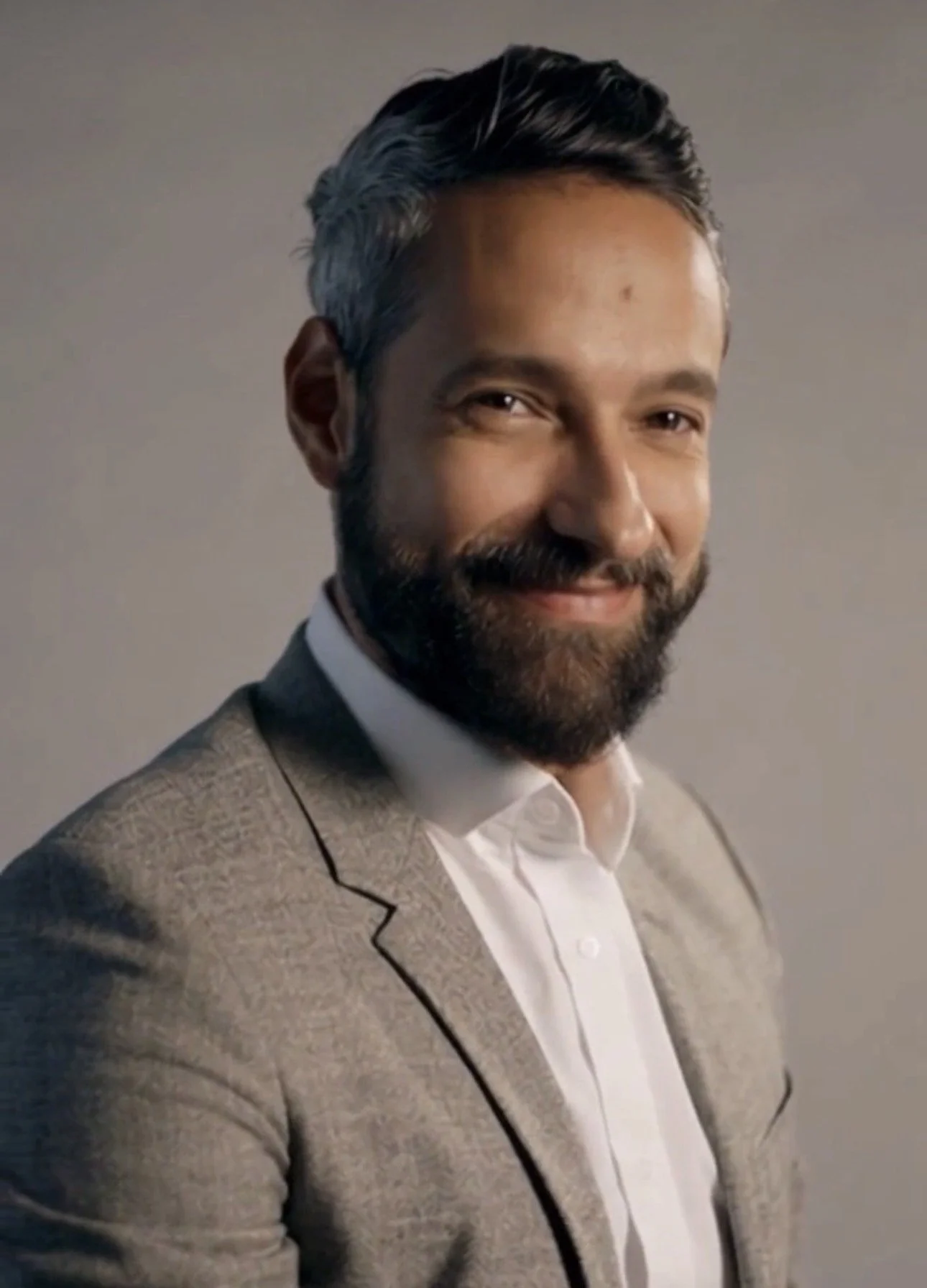 A tech leader and expert with dark hair, a beard, and a light skin tone, wearing a light gray blazer and white shirt, smiling at the camera against a neutral background.