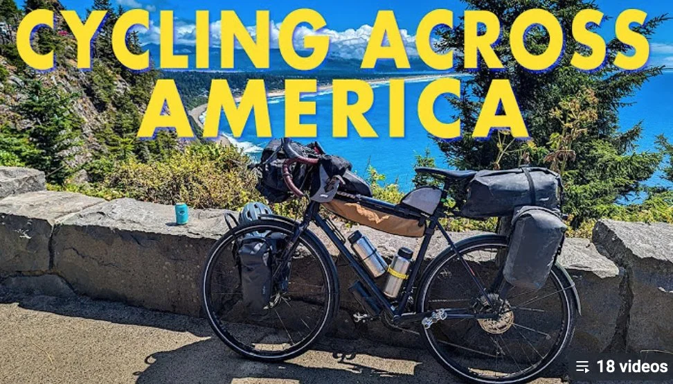 A bicycle loaded with gear parked on a scenic overlook with trees and a blue lake or ocean in the background.