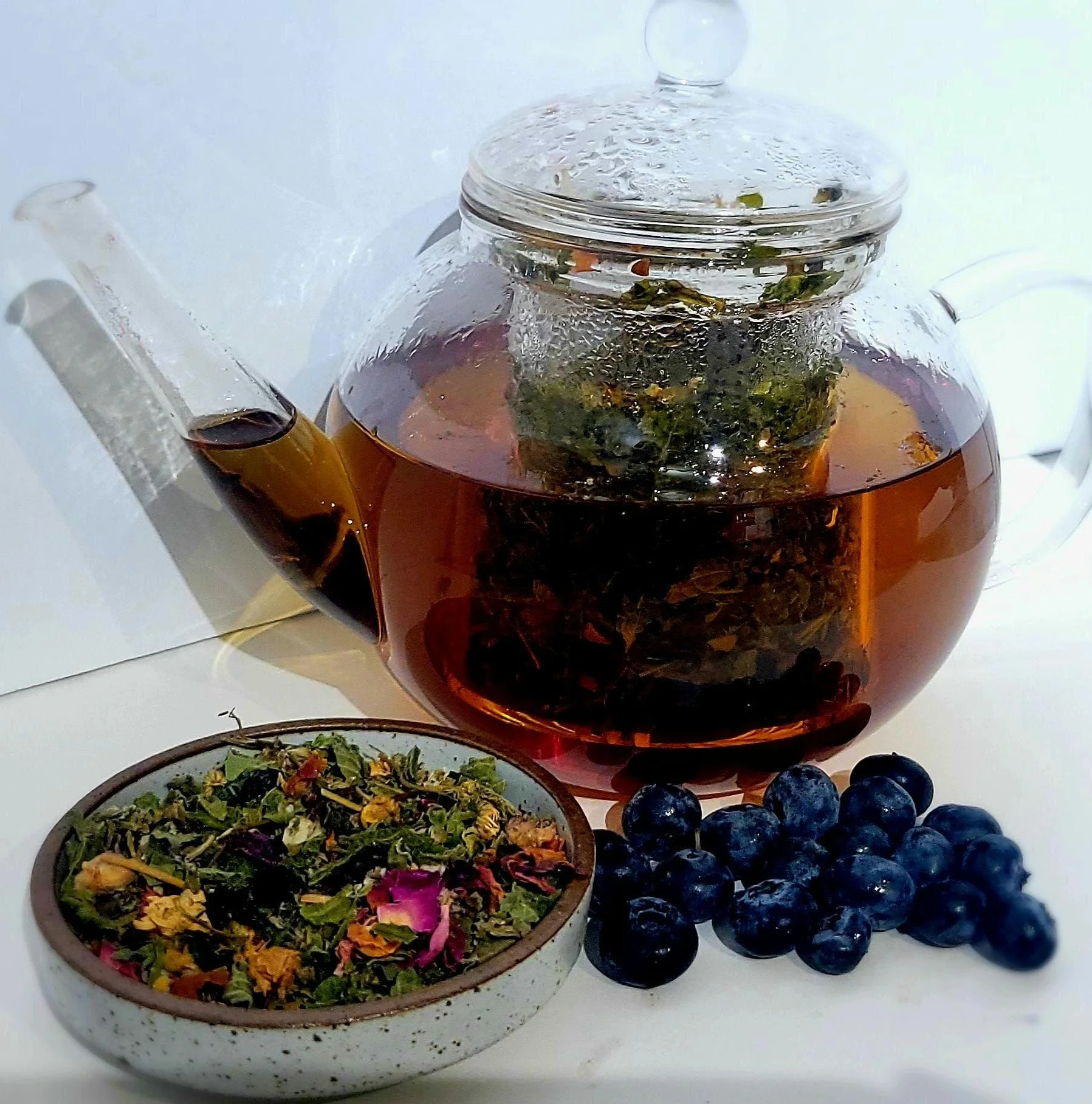 blueberry moon tea brewed in clear teapot with bluberries and dried tea small bowl display