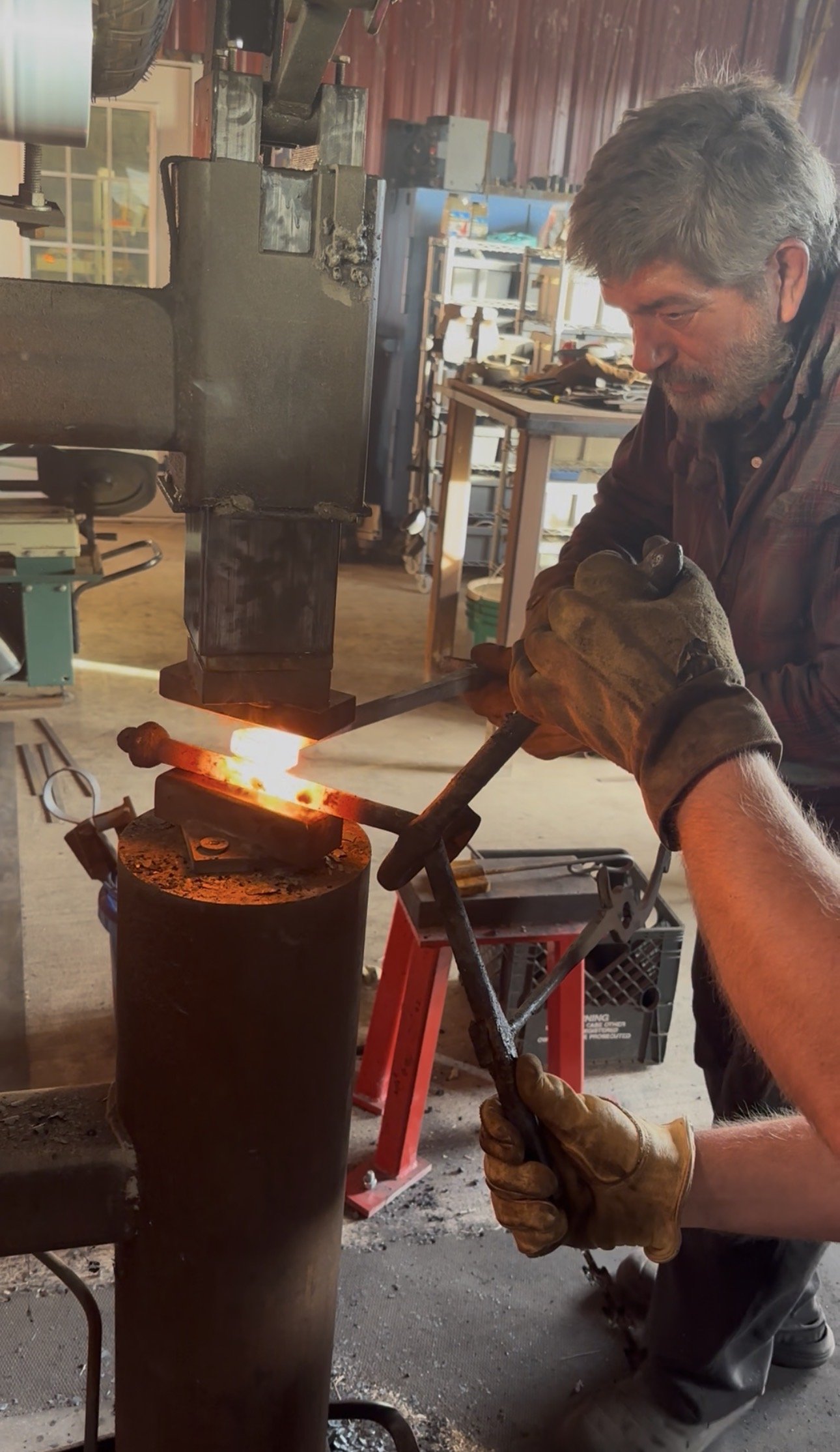 Blacksmith forging metal with a hammer and anvil, glowing hot metal piece in a workshop.
