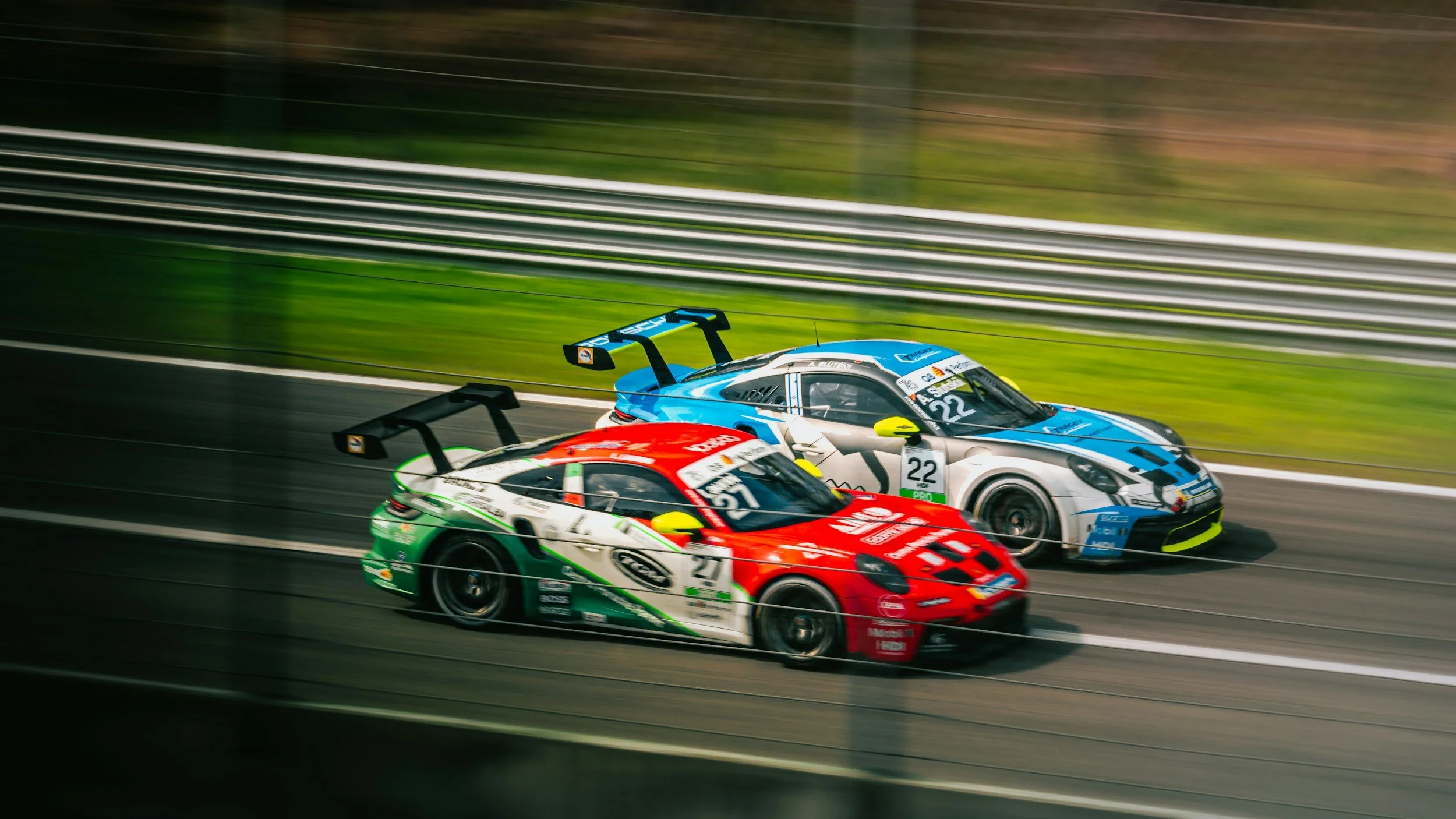 Two race cars, one red and white with green accents and the other blue and white, racing on a track.