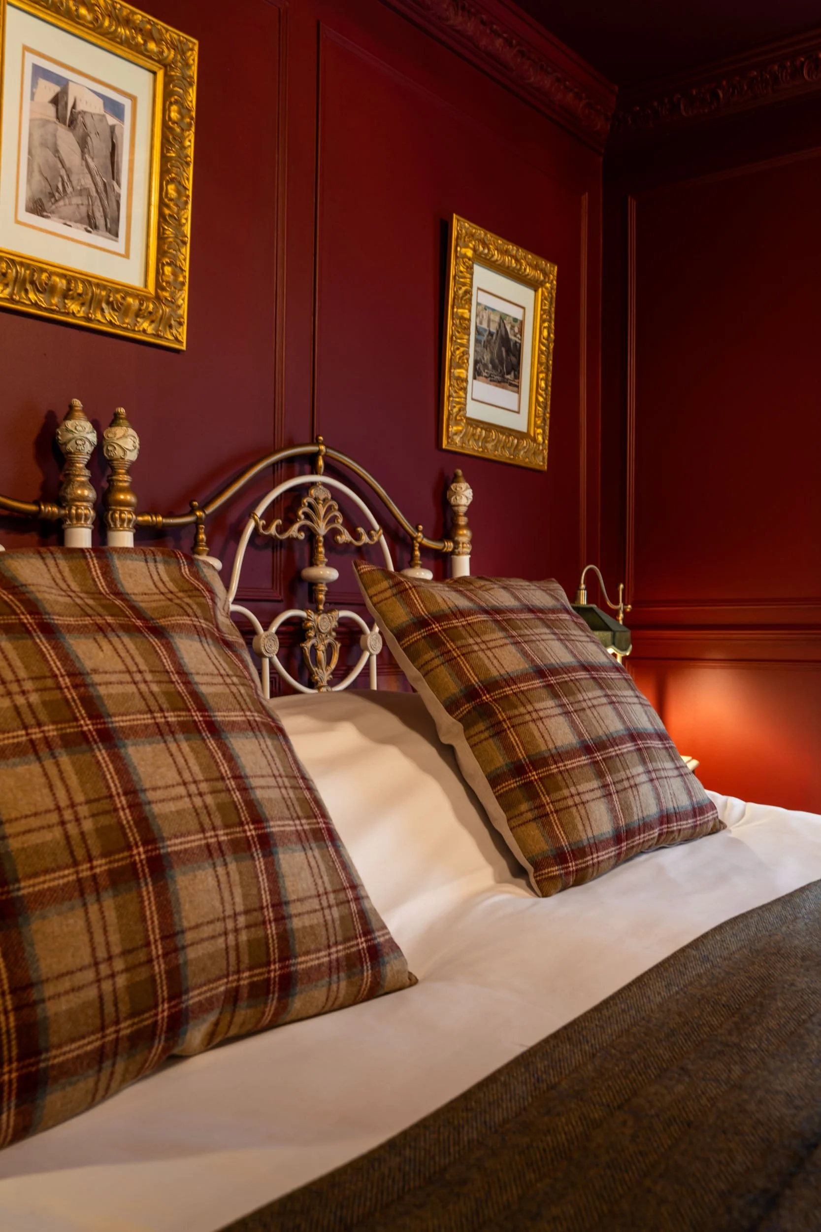 A cozy bedroom with a metal bed frame, plaid pillows, and a warm-toned wall decorated with framed artwork.