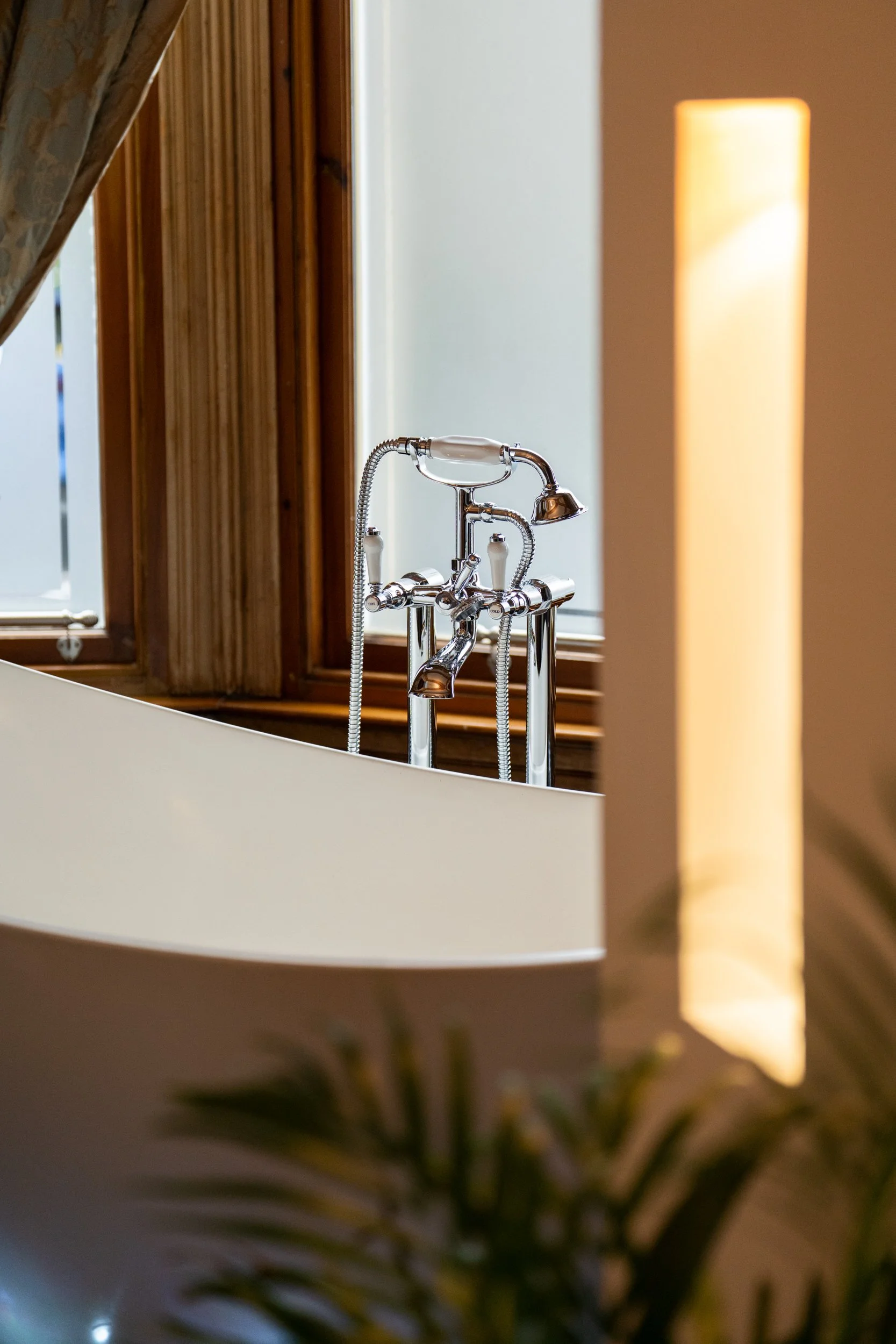 A vintage-style bathtub with a chrome faucet and handheld showerhead, near a window with wooden trim in a bathroom.