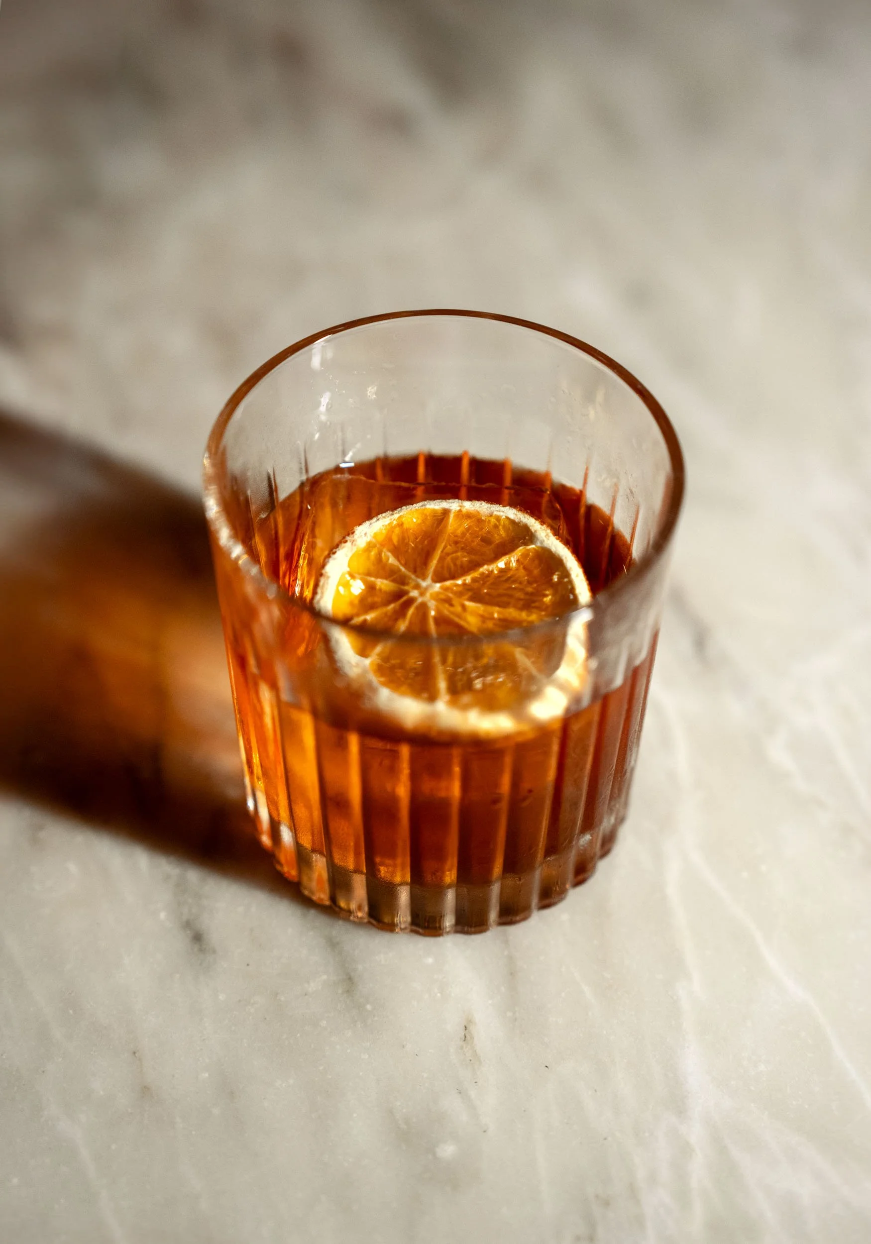 A glass of iced tea with a slice of lemon inside, placed on a light-colored marble surface.