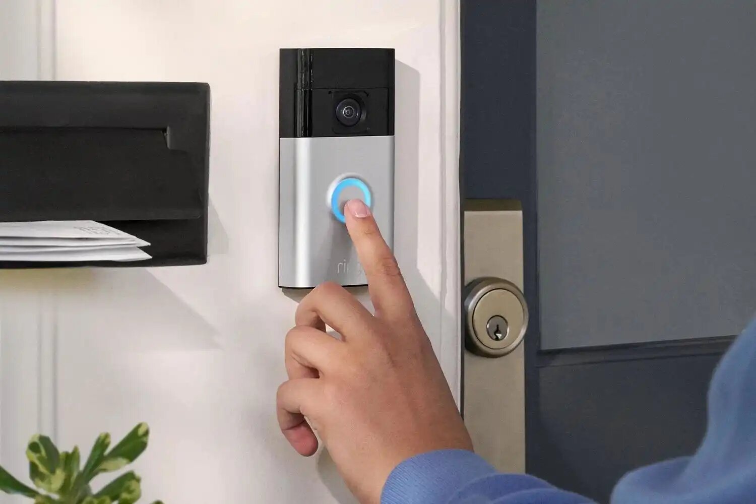 Person pressing a doorbell button with a blue light indicator next to a security camera and keyhole on a door.