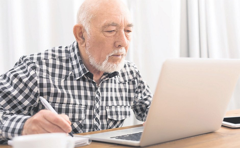 An elderly man with a white beard working on a laptop at a desk.