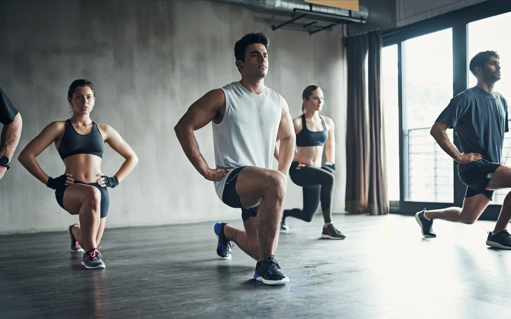 Group of people in athletic attire participating in a fitness class in a bright, modern studio with large windows.
