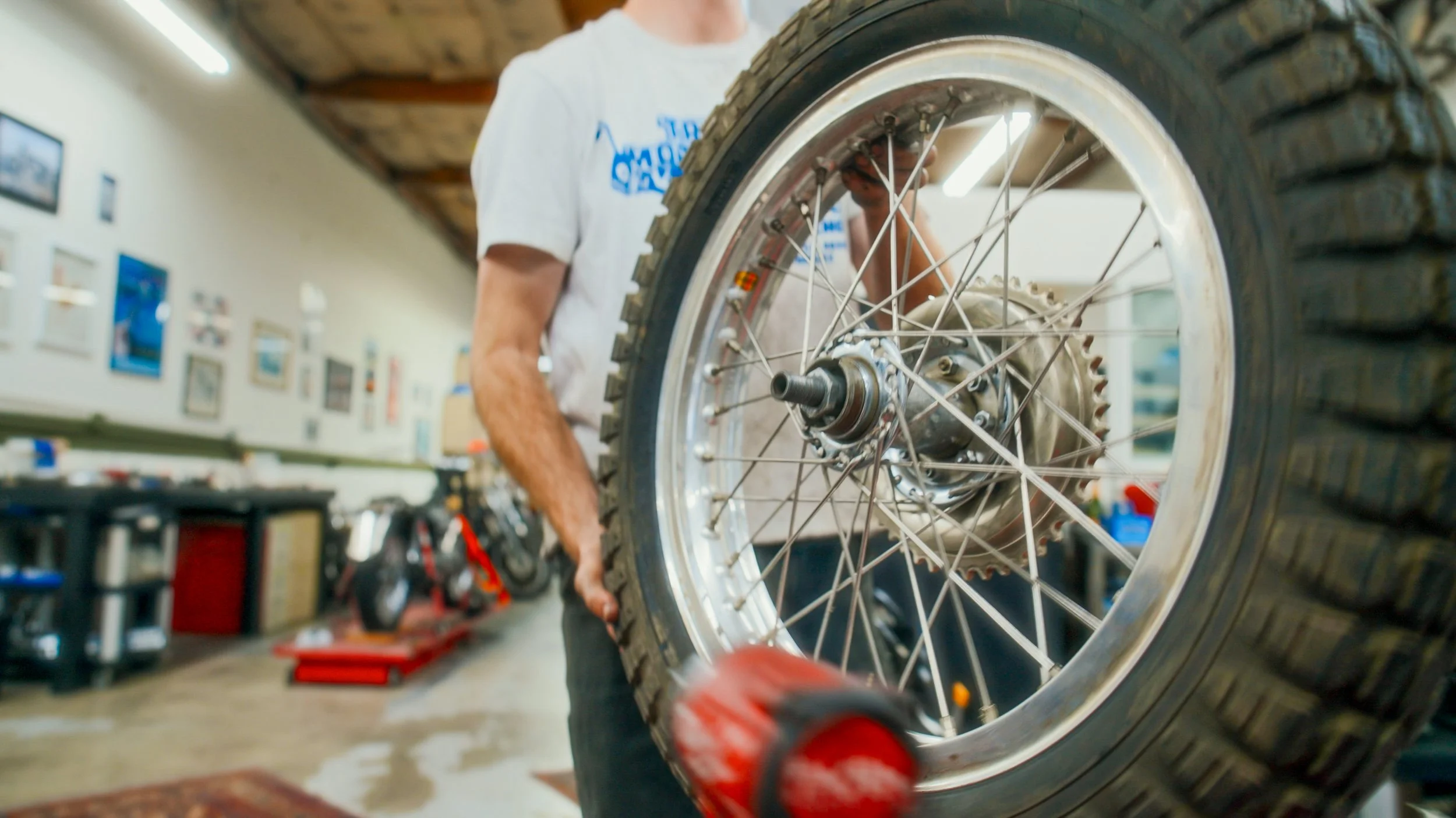 A person working on a motorcycle wheel in a garage, with tools and pictures on the wall in the background.
