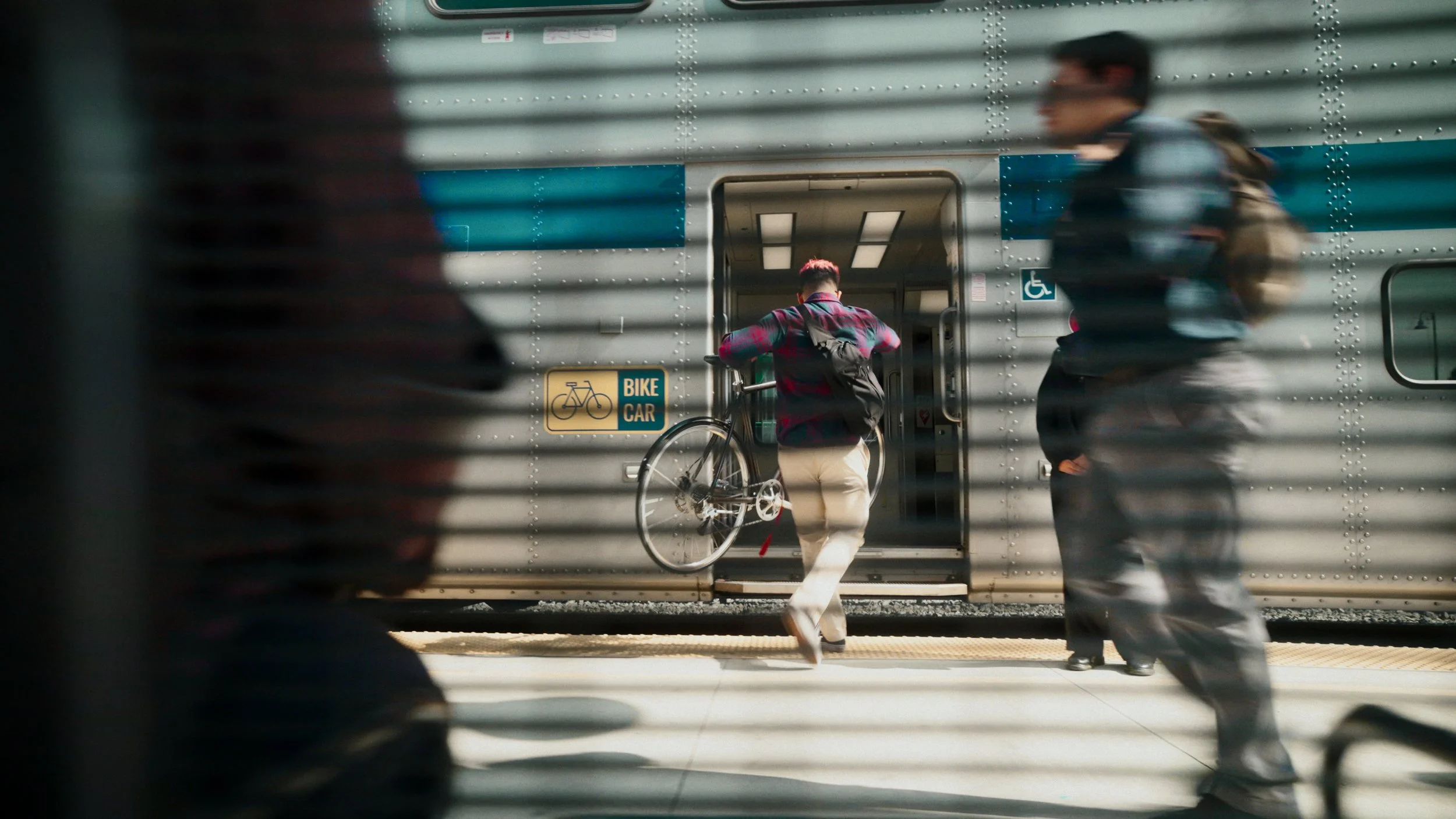 Person in a plaid shirt with a bicycle entering a train at a station, seen through a partially closed security shutter.