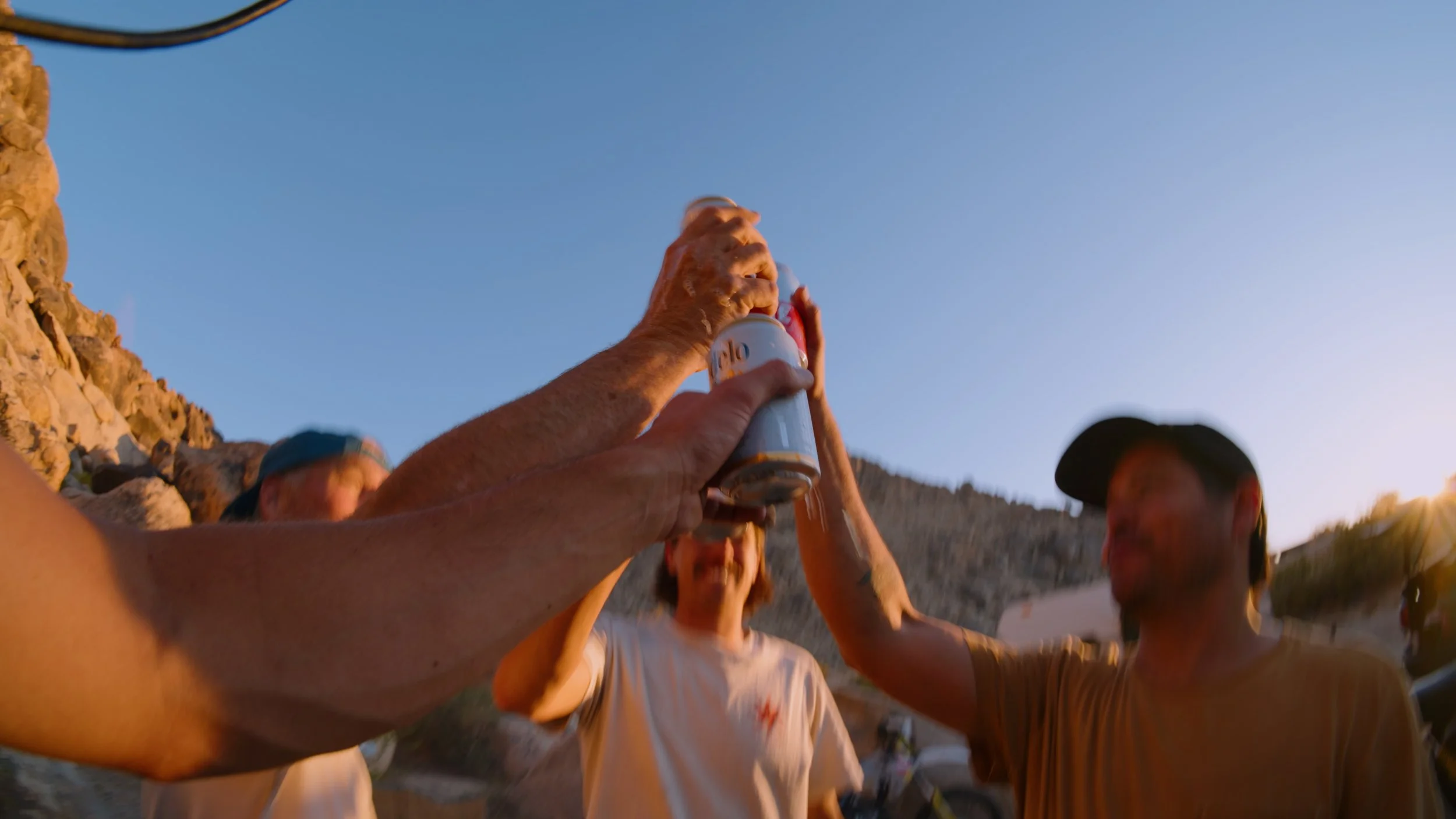 People raising drinks in a toast outdoors during sunset, with rocky terrain and clear sky in the background.