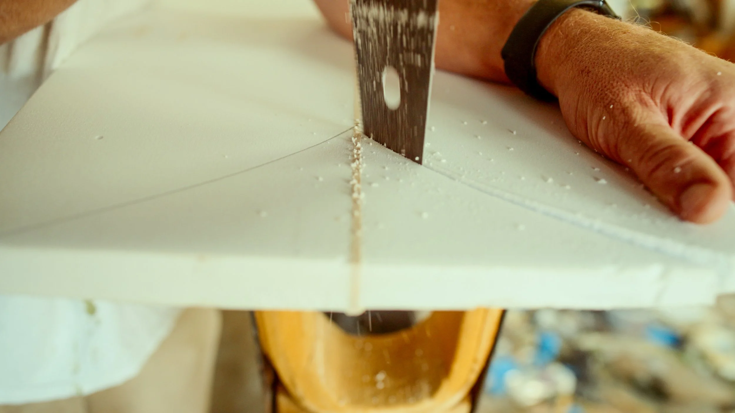 Close-up of a person cutting a large block of cheese with a long serrated knife.
