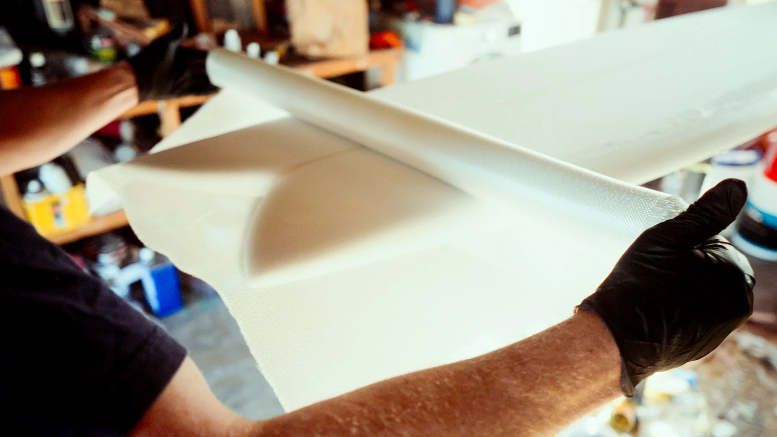 Close-up of a person wearing black gloves holding a large piece of white foam or insulation material in a workshop or garage environment.