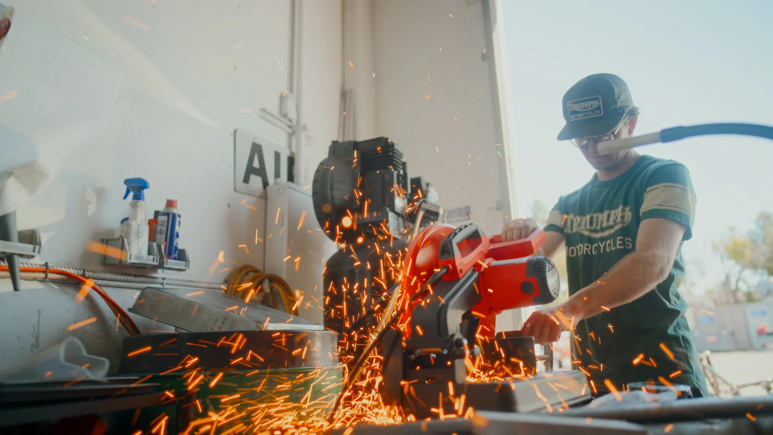 Man wearing glasses and a cap using a circular saw, cutting metal with sparks flying.