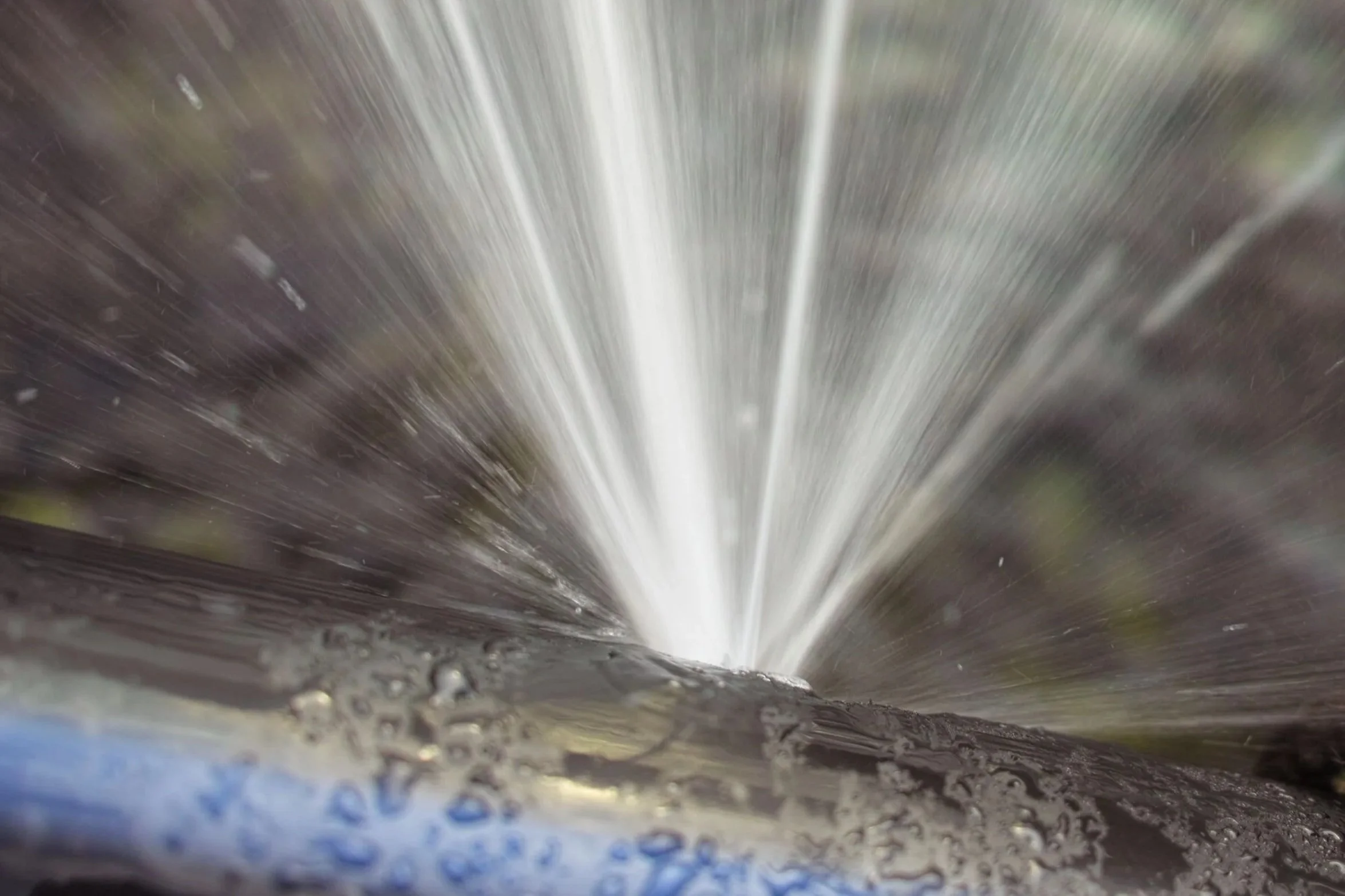 Close-up photo of water spraying downward, captured at high speed with a blurred background and bubbles at the bottom of the image.