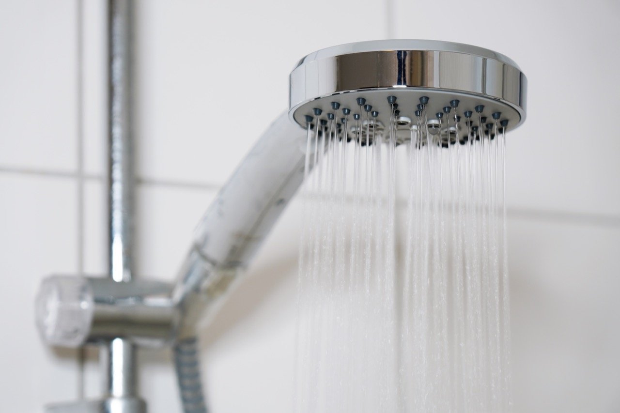 A chrome showerhead with water flowing out in a bathroom.