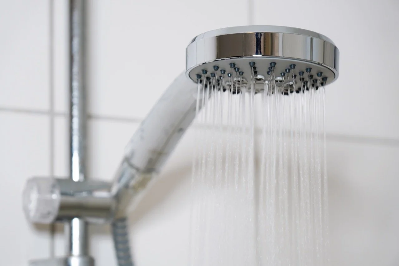 Close-up of a modern chrome showerhead with water streaming out in multiple thin lines.