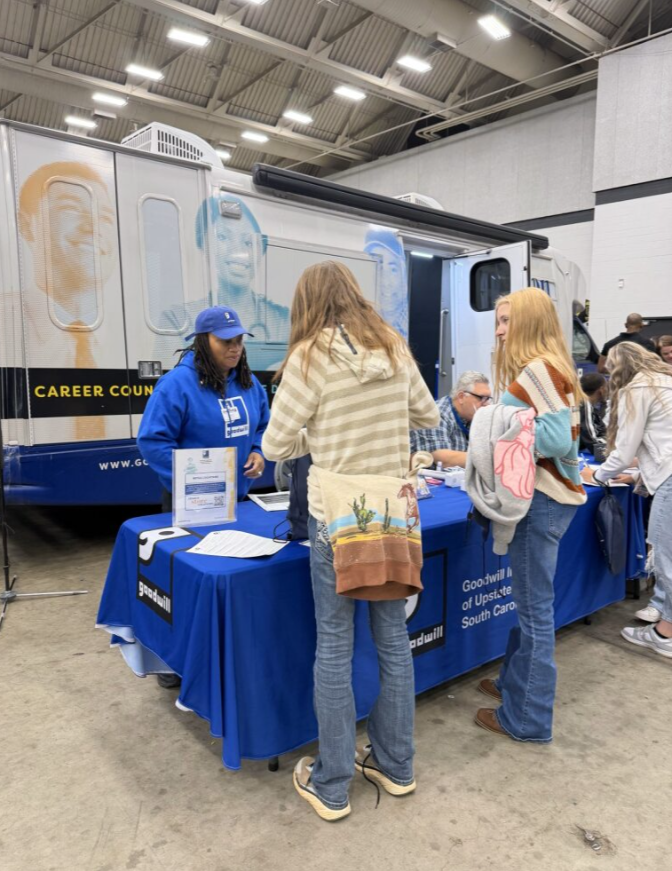 People at a career fair booth with a bus display in a large indoor venue.