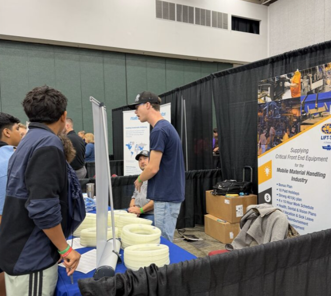 People at a trade show booth with stacked coiled cables and informational banners.