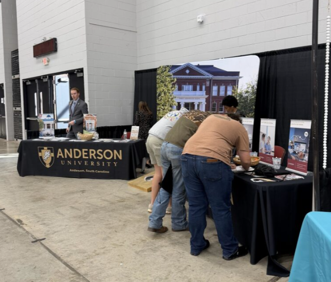 Anderson University booth at an indoor event, with several people exploring informational materials and brochures.