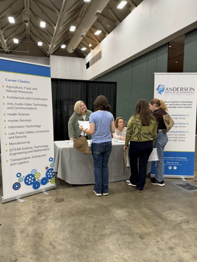 People gathered around a booth at an educational or career fair, with banners listing various career clusters and information about Anderson Institute of Technology.