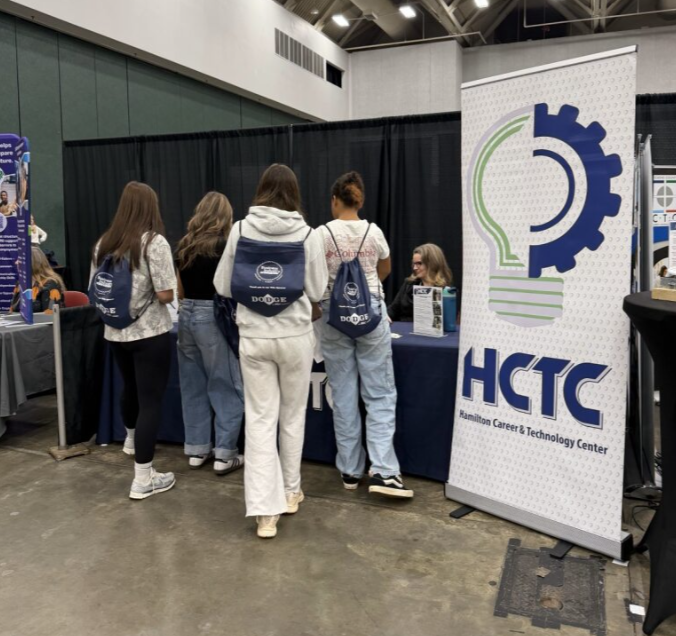 Group of people visiting a booth at a career and technology fair with HCTC banner and informational materials.