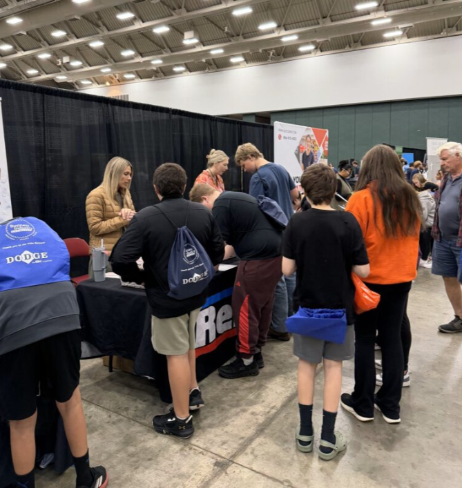 People gathered at a registration table at an indoor event, with posters and vendors in the background.