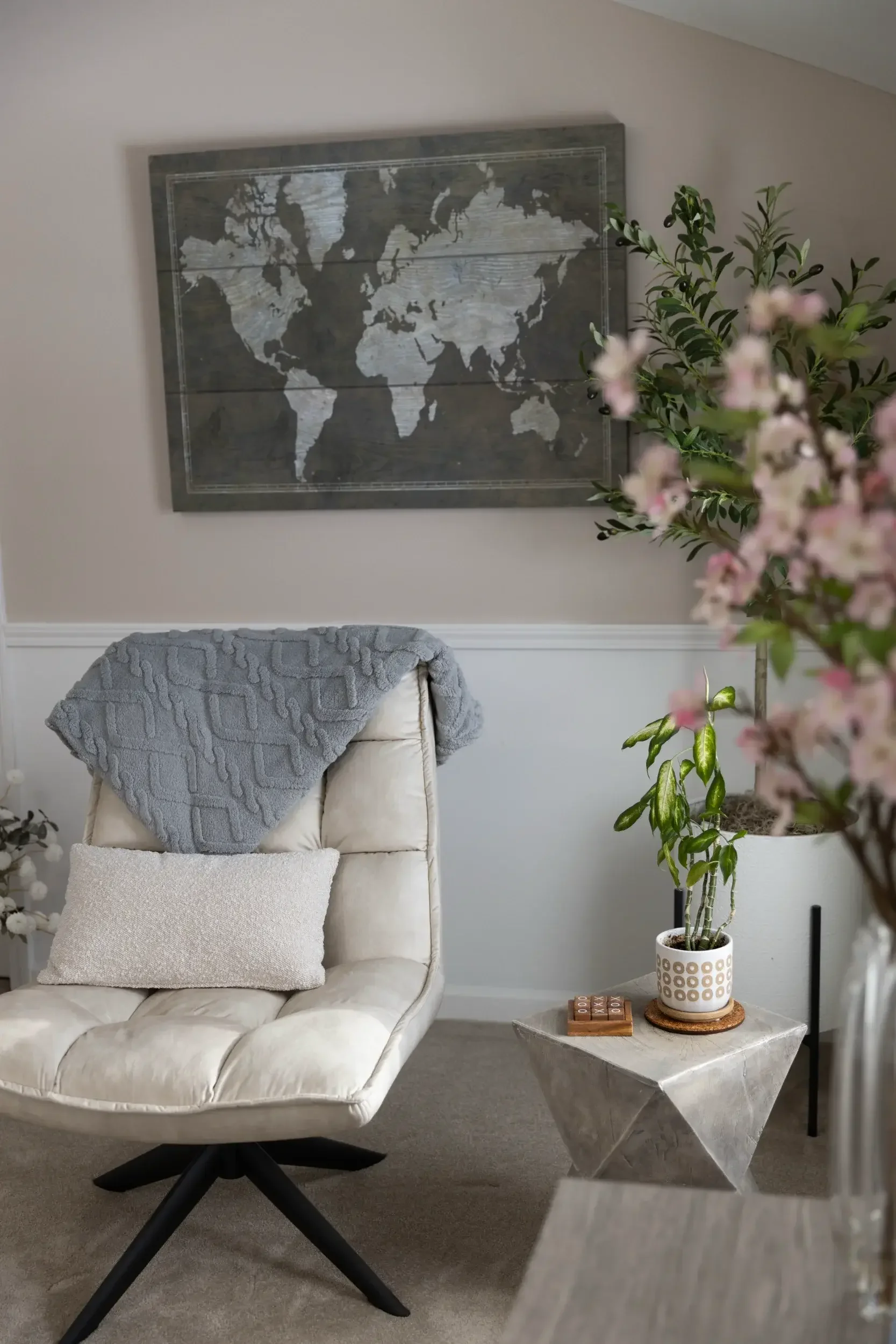 A cream colored office chair beneath a taupe wall with a wooden map of the world hung on it.