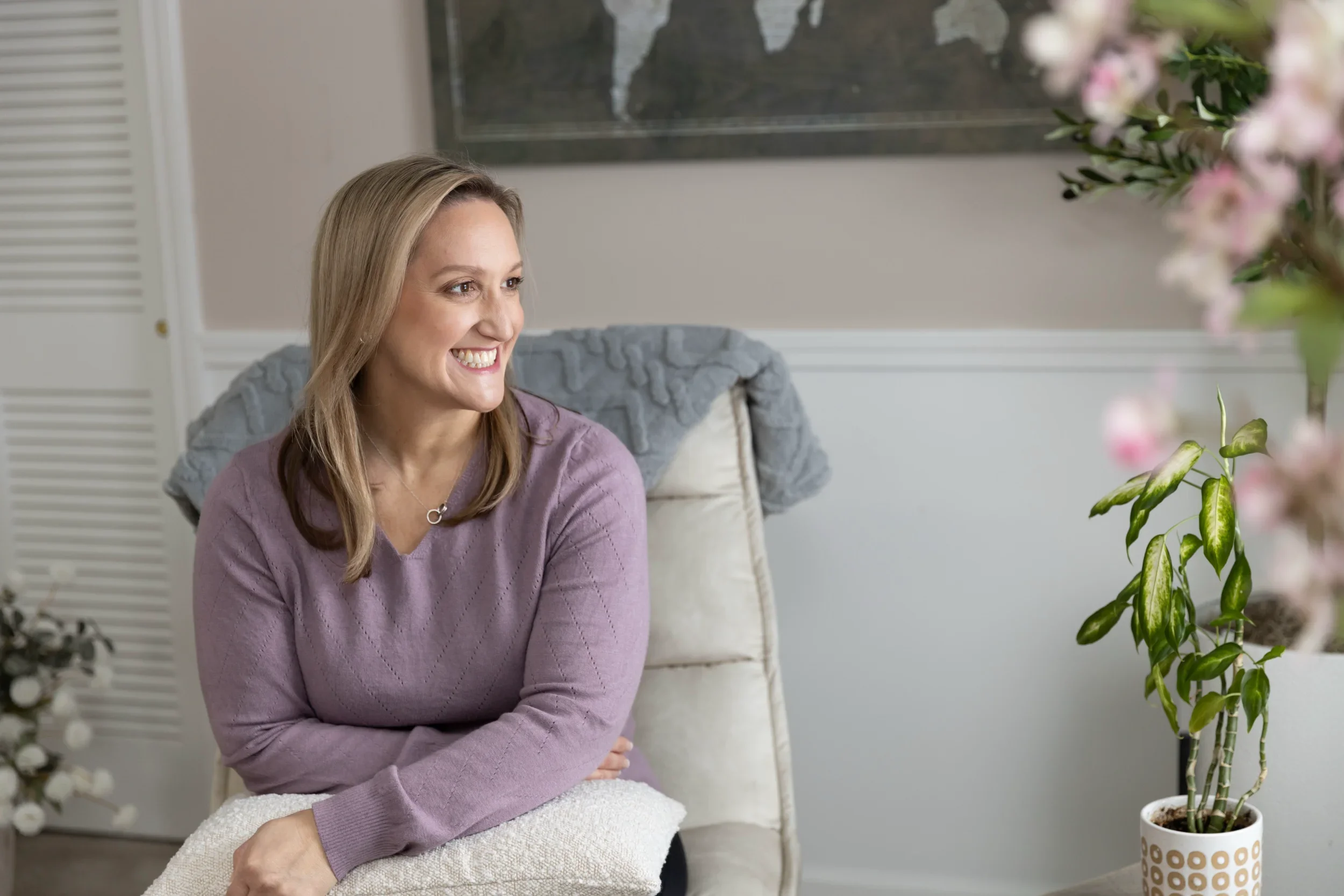 Tina sitting in a cream-colored chair wearing a purple sweater. She is looking to her left and smiling.