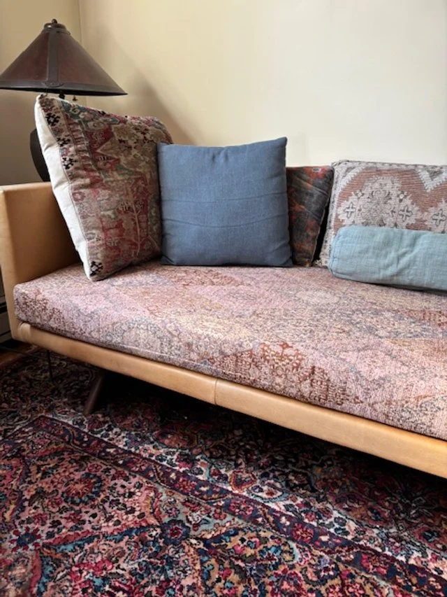 Living room sofa with patterned cushions and a floral rug underneath, next to a side table with a lamp.