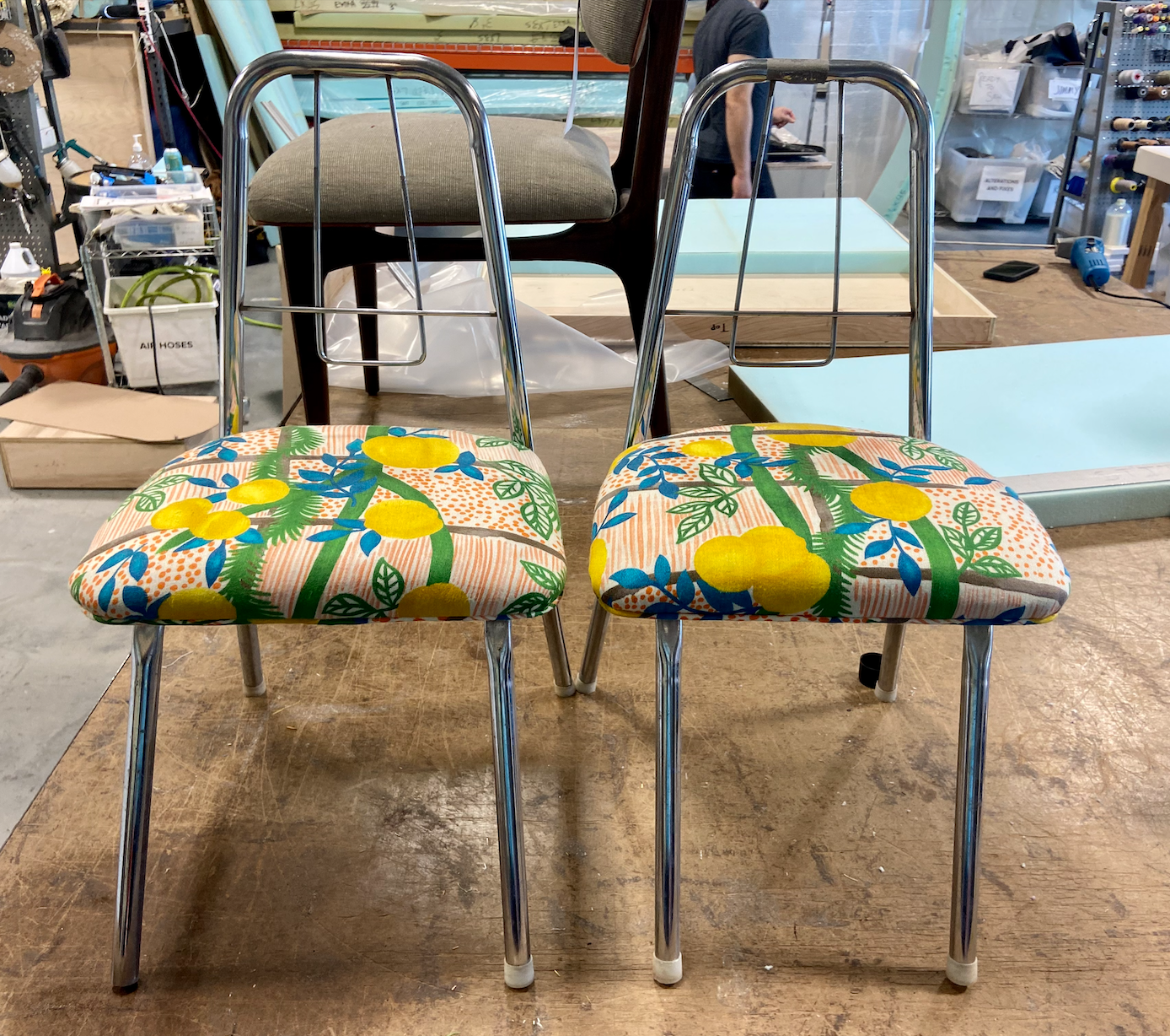 Two chairs with chrome legs and floral-patterned cushions featuring lemons and greenery, in a workshop.
