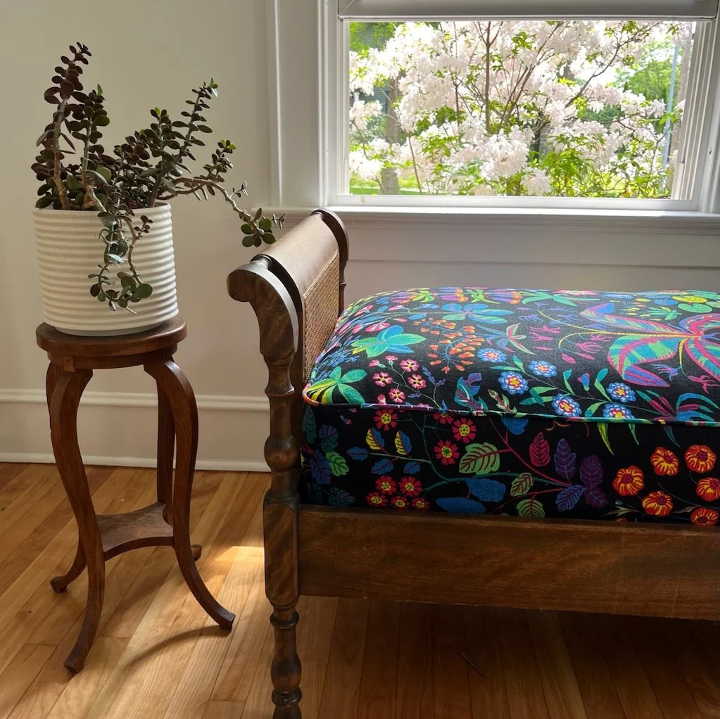 A wooden bench with a colorful floral-patterned custom cushion near a window.