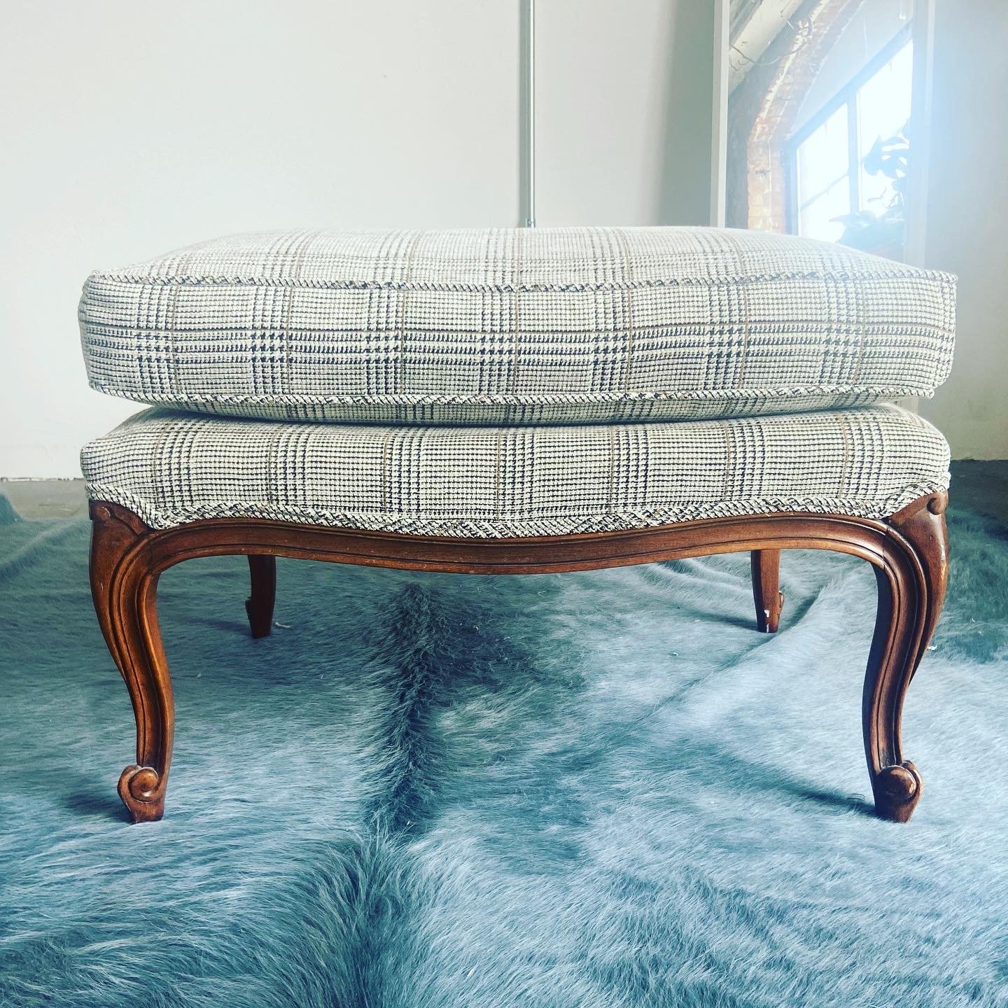 A vintage wooden-legged chair with a plaid cushioned seat placed on a light-colored rug near a window.