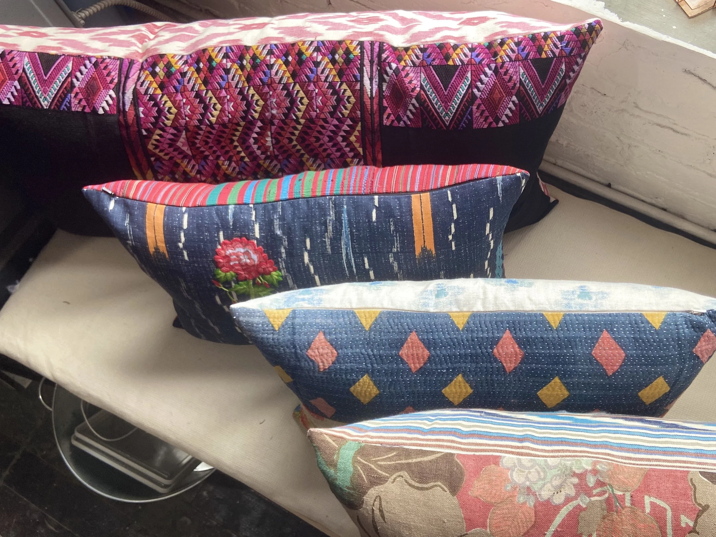 Four decorative pillows with colorful, patterned fabric on a beige cushion, placed on a bench.