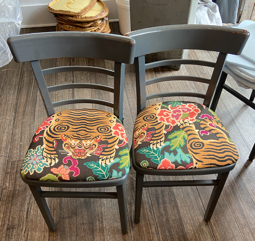 Two black wooden chairs with tiger and floral embroidered cushions on a wooden floor.